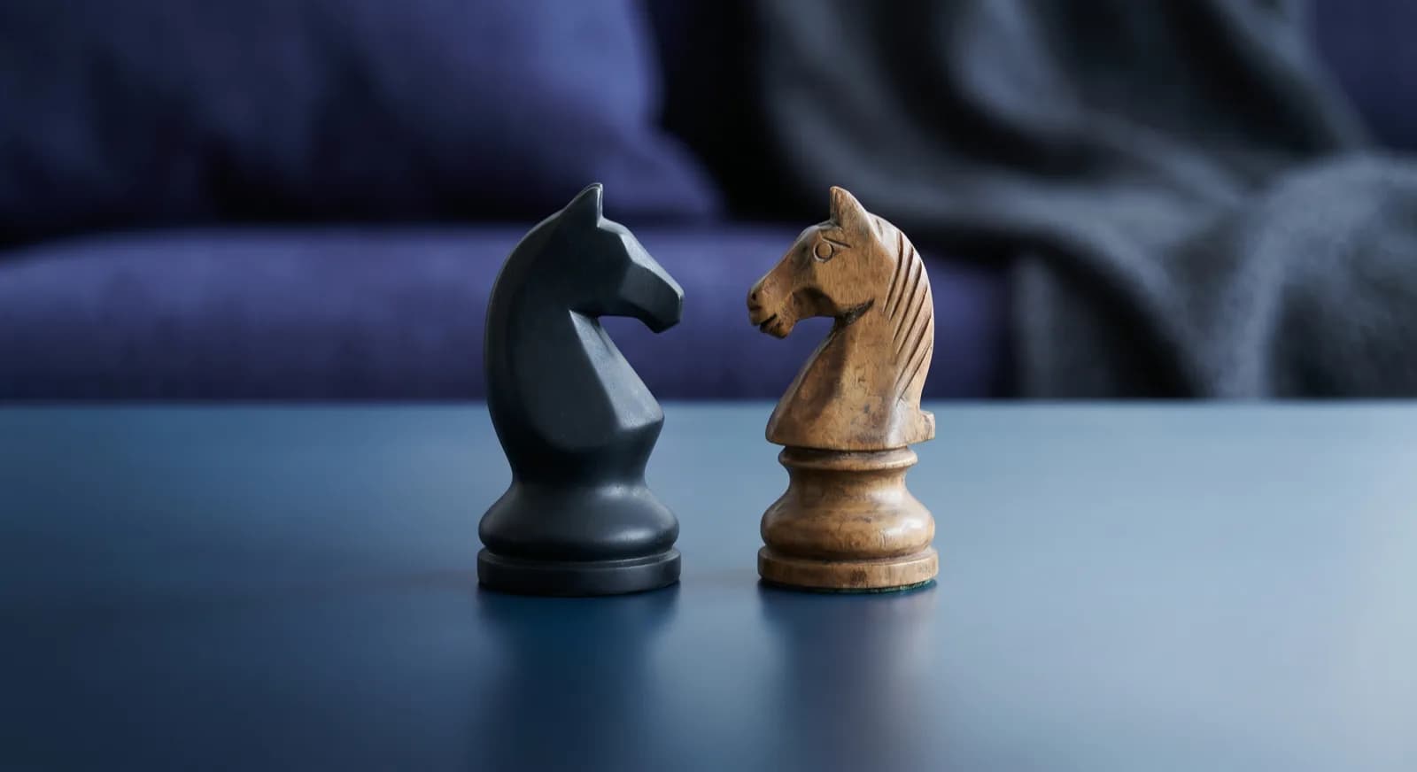 A modern black chess knight and a classic wooden knight facing each other