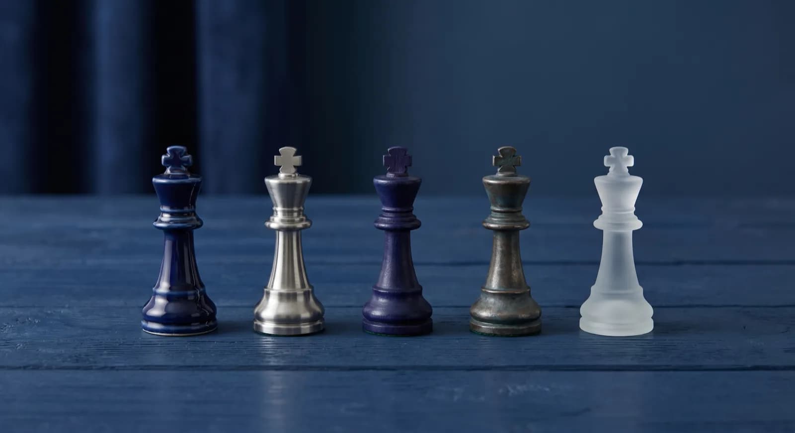 Five chess kings from different chess sets lined up in a row on a table