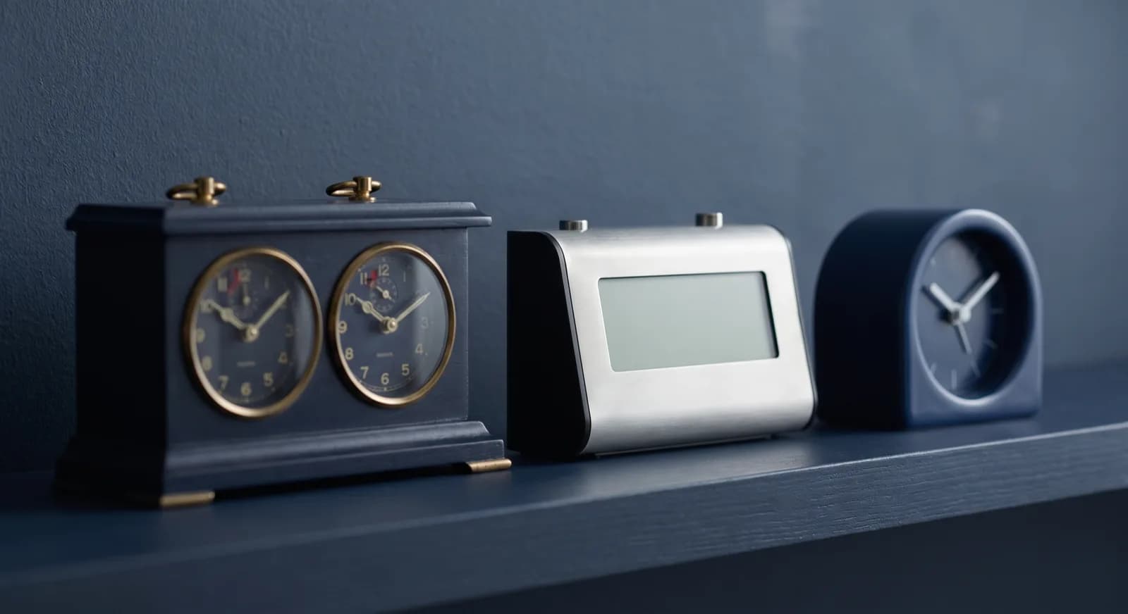 Three chess clocks of different designs lined up on a navy shelf